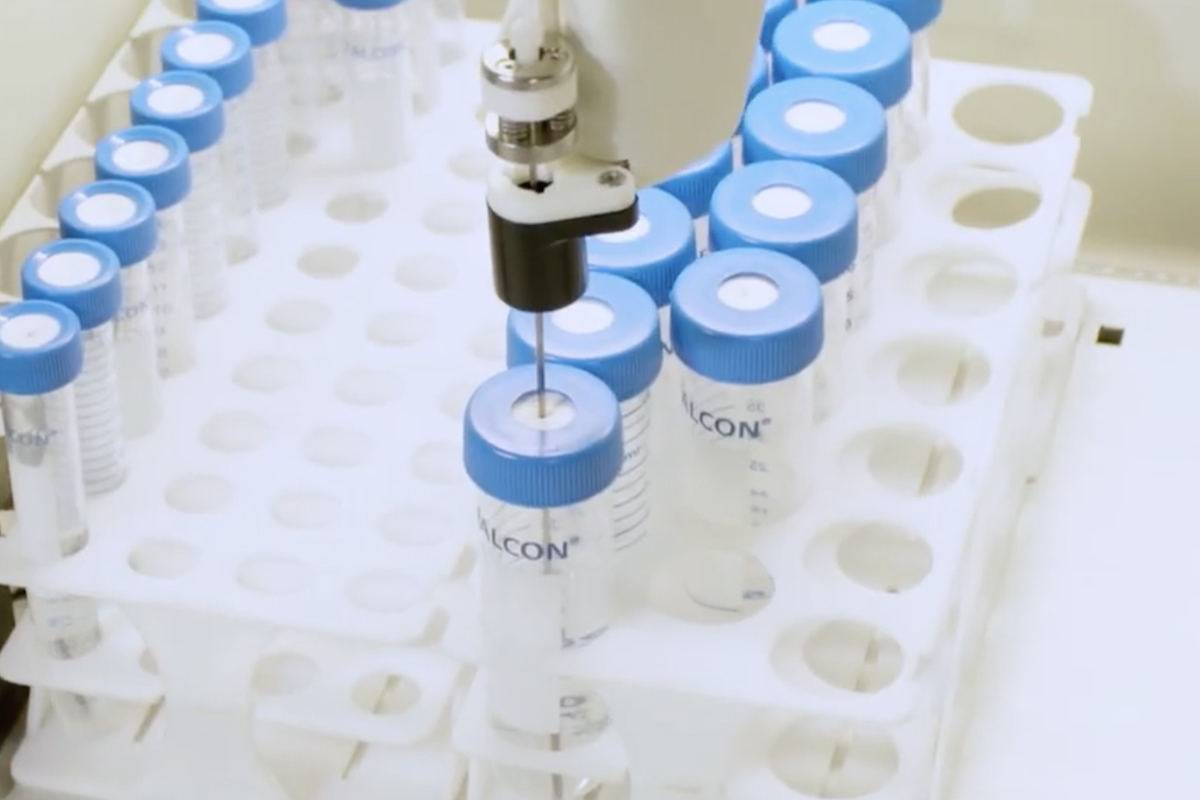 Automated probe piercing a blue septa cap An automated sampling probe piercing the white septum of a blue cap on a clear Falcon centrifuge tube, situated in a white rack among other capped tubes.